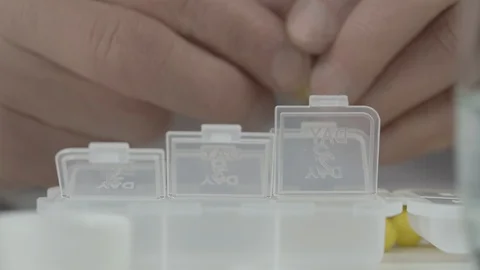 Old man puts pair of bright yellow pills into each section Stock Footage 126759585