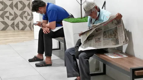 Old Man Reading Newspaper And A Young Man Looking At Mobile Phone Stock-Footage 154072111