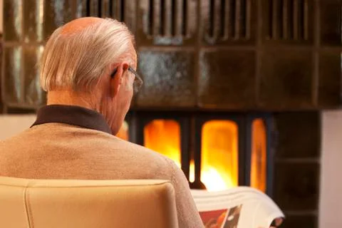 Old man reading newspaper while sitting by a fireplace in a living room Фото
