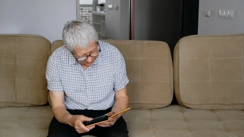 Old man retired sitting on the couch and watching photos Stock Footage 111527774
