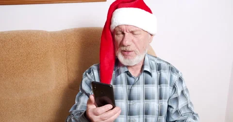 Old man in a Santa hat chatting on a video call using a smartphone at home Stock Footage 147051284