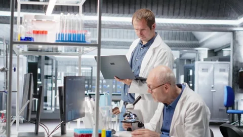 Old man scientist using microscope with a colleague for clinical study Stock Footage 317789572