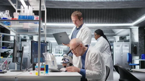 Old man scientist using microscope with a colleague for clinical study Stock Footage 317790606