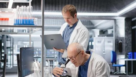 Old man scientist using microscope with a colleague for clinical study Stock Photos