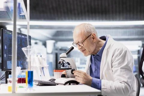 Old man scientist using microscope instrument in clinical research study Stock Photos