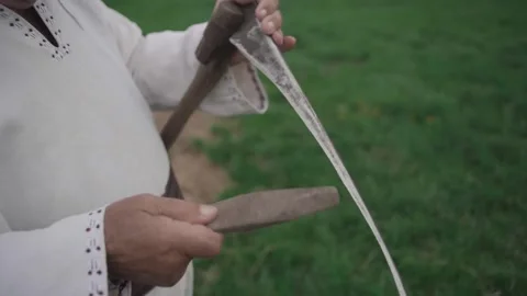 Old man sharpens an old scythe in the field Stock Footage 298869827