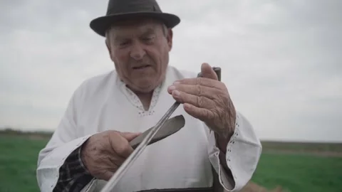 Old man sharpens an old scythe in the field Video stock 298870032