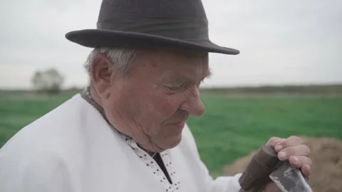 Old man sharpens an old scythe in the field. Look into the camera Video stock 298870066