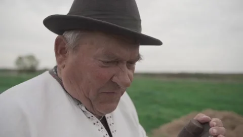 Old man sharpens an old scythe in the field. Look into the camera Stock Footage 298870083