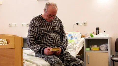 Old man sits hosp bed read book Stock Footage 81836945
