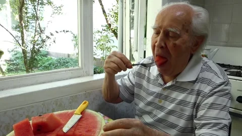 Old man sits in the kitchen and eats watermelon with his hands. Stock-Footage 137131727