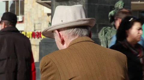 Old man sitting alone. Lonely elder sitting on a bench, people walk past him. Stock Footage 33036882