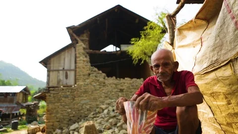 Old man sitting and wearing his cap in front of a village backdrop Stock Footage 77444489