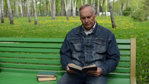Old man sitting on the bench in the park and reading a book Stock Footage 72077155