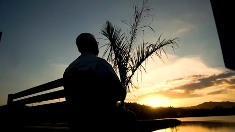 Old man sitting on bench watching the sunset 動画素材 103803708