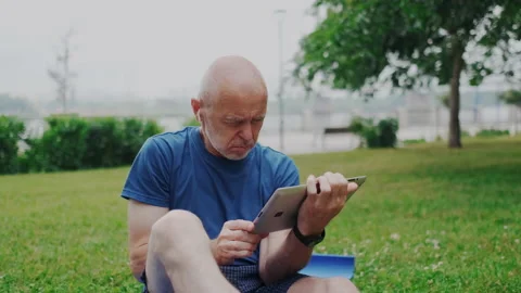 Old man Sitting on Grass in Park Outside and Using Wireless Tablet PC. Retiree Stock Footage 148467566