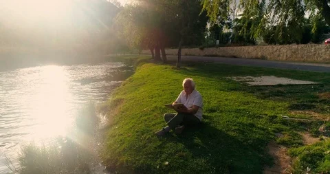 Old man sitting reading in the field Stock Footage 124381692