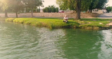 Old man sitting reading by river Stock Footage 124381868