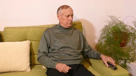 Old man sitting on the sofa and switching on tv with remote control Stock Footage 71894260