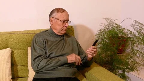 Old man sitting on sofa in the living room and using his cellphone Stock Footage 71895108