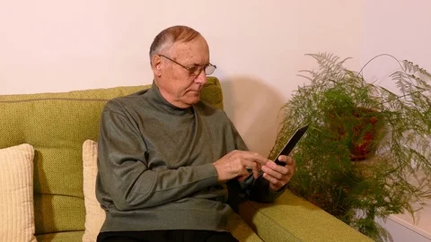 Old man sitting on sofa in the living room and using his phone Stock Footage 71895617