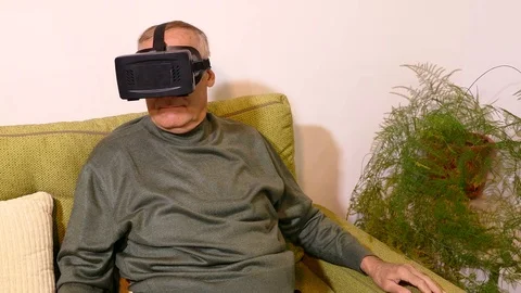 Old man sitting on the sofa in the living room and using virtual glasses Stock Footage 71896375