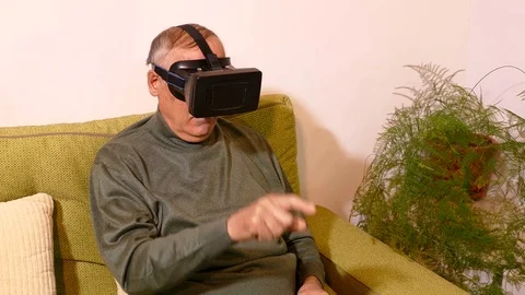 Old man sitting on the sofa in the living room using virtual glasses Stock Footage 71896448
