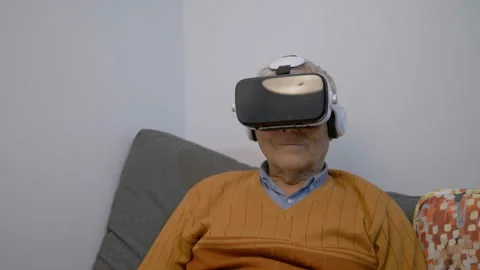 Old man sitting on sofa with virtual eyeglasses, old man and new technology  Stock Footage 141357550