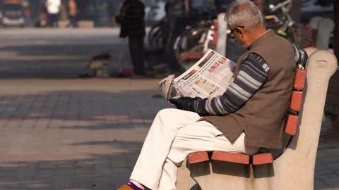 Old man sitting on sunny park bench reading newspaper in sector 17 market in Stock Footage 234989202