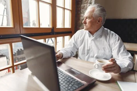 Old man sitting at the table and working with a laptop Stock Photos