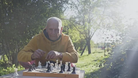 Old man sitting at table in garden and playing in chess game with yourself Stock Footage 251489001