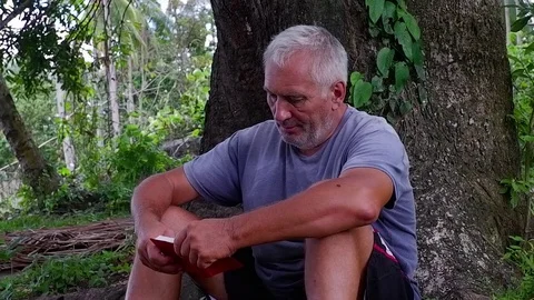 An old man sitting under the tree while reading a book. Video stock 122476953