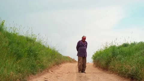 Old man in a skullcap stands and look in the camera on the country road Vídeos de archivo 194545112