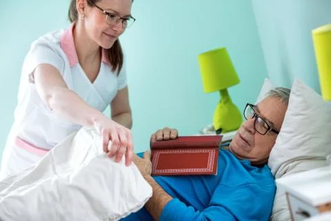 Old man sleeps while reading a book, nurse cover him with blanket Stock Photos