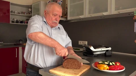 Old man slices rye bread with big grey steel knife on board Stock Footage 108605686