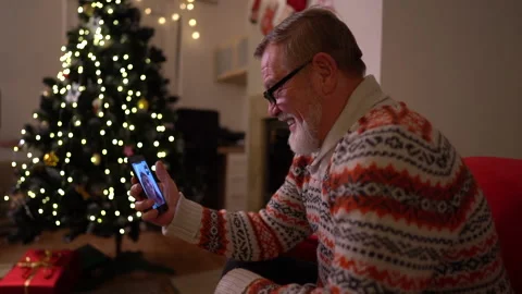 The old man with a smartphone make a video call near the christmas tree Video stock 143863825