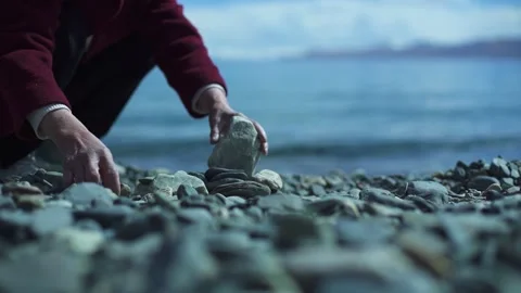 Old man stacking stones by the river Video stock 243064878