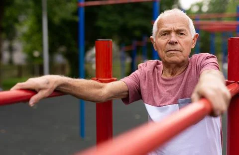 Old man standing between parallel bars outdoors Stock Photos