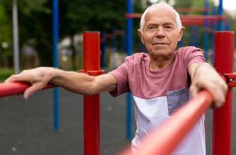 Old man standing between parallel bars outdoors Stock Photos