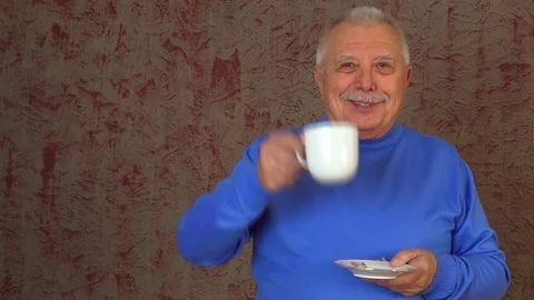 Old man stands against red wall and drinks hot green tea Stock Footage 108605072