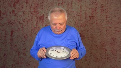 Old man stands against wallpaper holds clock and rejoices Stock Footage 108605053