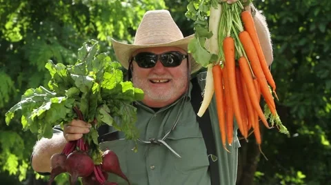 Old man with straw hat and sun glasses lifts up carrots and radish to camera Stock Footage 45524640