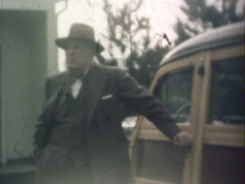 Old man in suit and hat leaning on car smoking - vintage 8mm Stock Footage 79174832