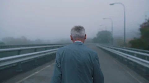 An old man in a suit walks along an empty road in cloudy weather Stock Footage 144576747