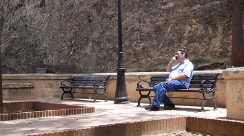 OLD MAN TALKING ON CELLPHONE on bench in small park - Old San Juan. Puerto Rico Stock Footage 51331515