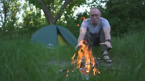 Old man tourist  warms hands near tent camping with fire. Slow motion Stock Footage 156041085