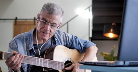 Old man is training to play guitar watching tutorial online 스톡 동영상 138938424