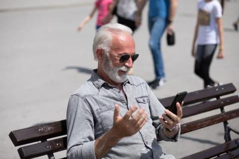 Old man use internet application on smartphone, seating on bench,  stock phot Stock Photos