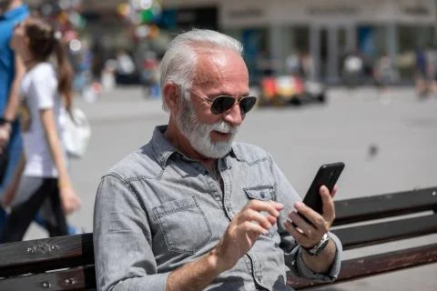 Old man use internet application on smartphone, seating on bench,  stock phot Stock Photos
