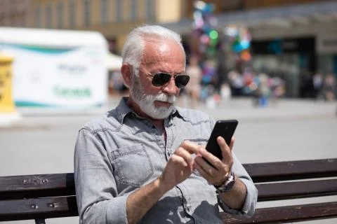 Old man use internet application on smartphone, seating on bench,  stock phot Stock Photos